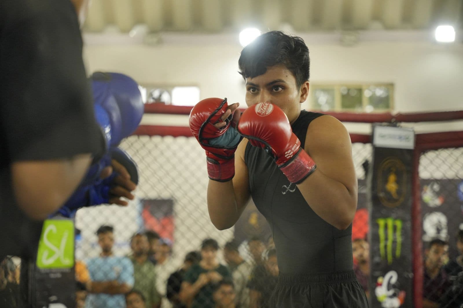 A female fighter in red MMA gloves holds her guard inside the cage, Devils Octagon Season Two